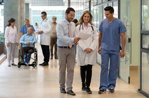 three health care professionals standing close together in hospital hallway while reviewing clinicals